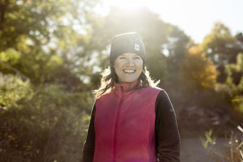 smiling woman in warm outdoor clothing backlit by sun on autumn day