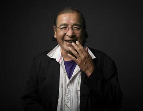 smiling Indigenous man with hand raised to mouth in laughter