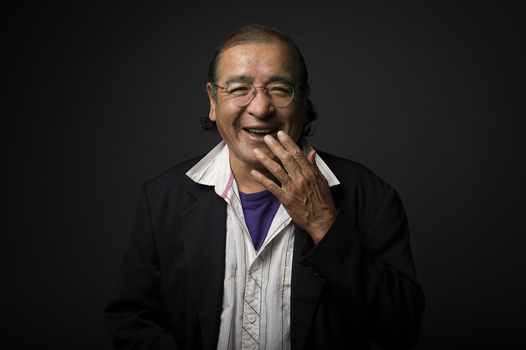 Smiling indigenous man wearing a jacket and shirt, with hand held to mouth in laughter