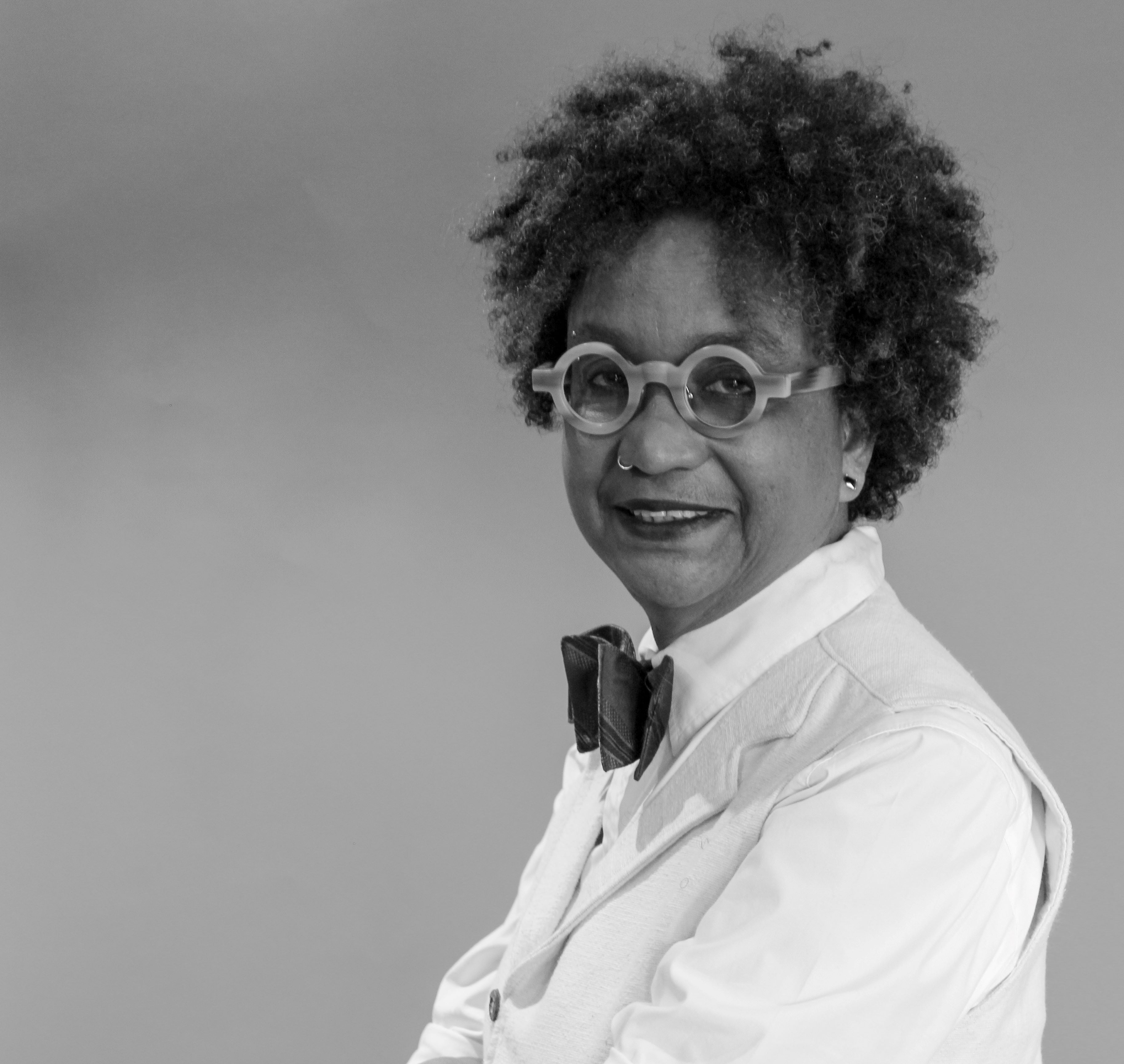 Person with curly hair and round glasses wearing dress shirt with bowtie in black and white