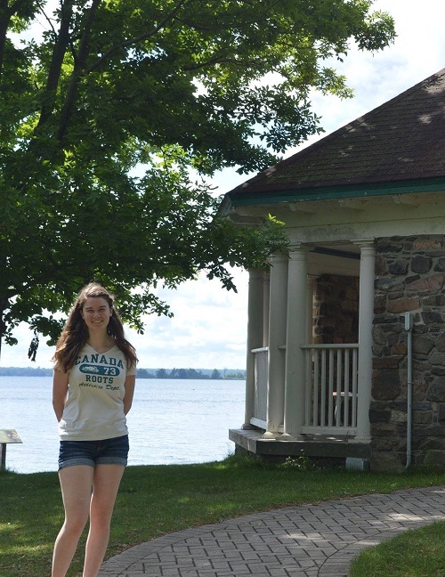 Smiling person standing in front of tree and historic building by lake in summer