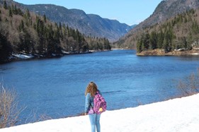 Person standing in snow, overlooking lake and wooded hills in distance