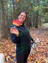 Smiling young person standing in forest holding autumn maple leaf to camera