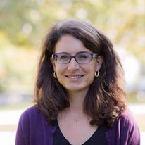 smiling human with glasses facing camera backed by sunlight. 