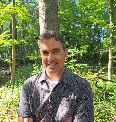 human smiling into camera while in middle of woods