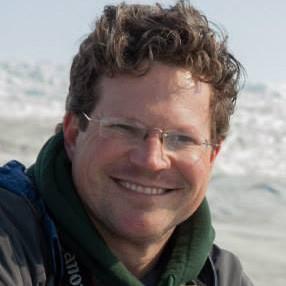 smiling person with glasses facing camera in arctic landscape