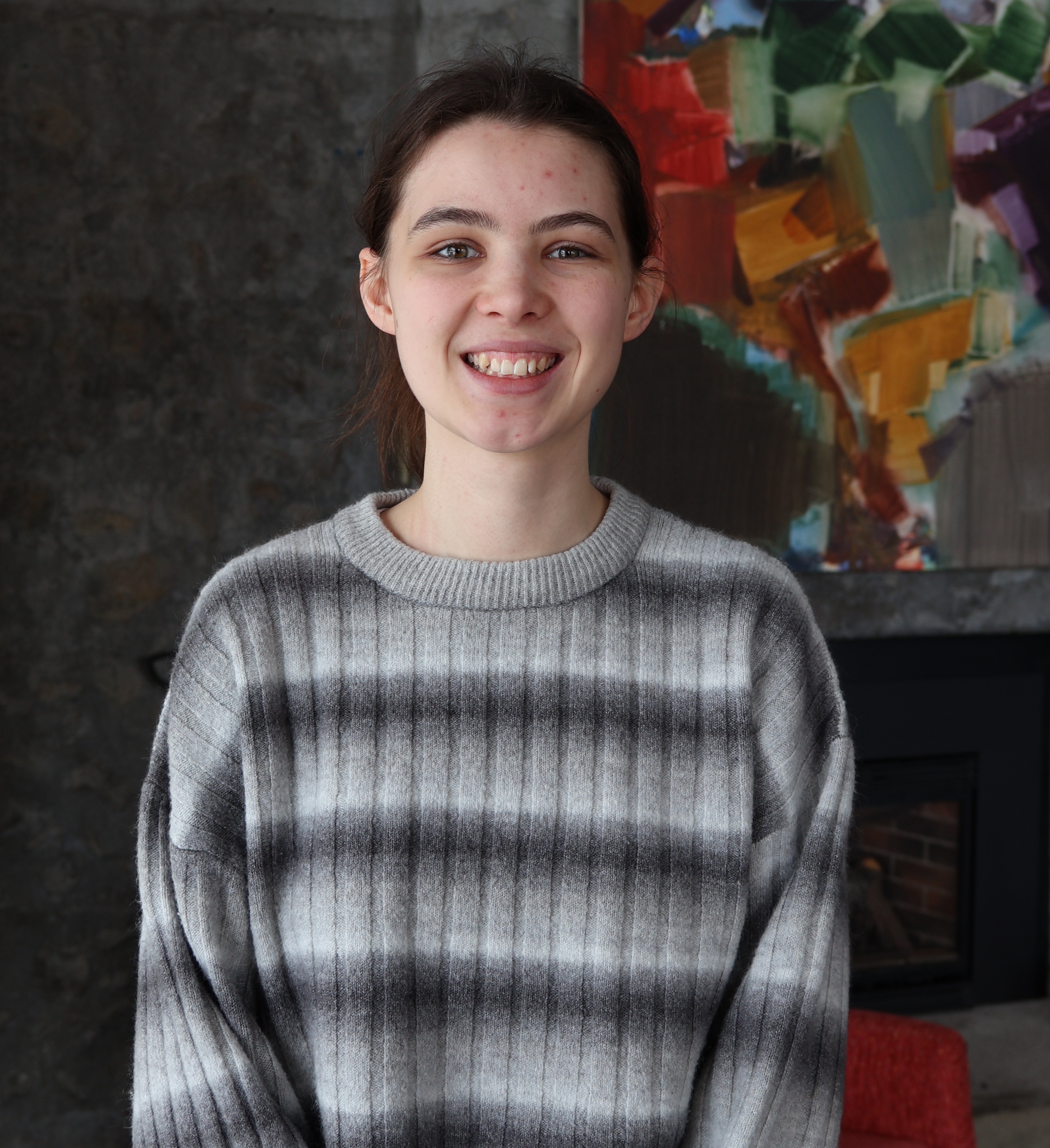 Co-op student smiling at the camera. The background features an abstract painting hung over a fireplace