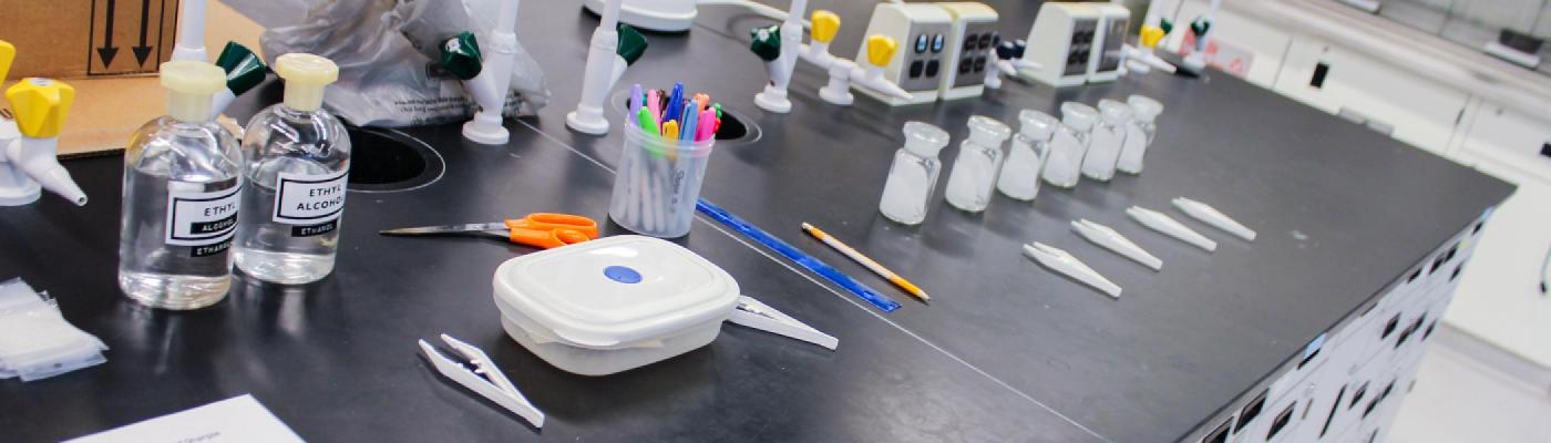 A chemistry lab work bench with solvent bottles, markers, and TLC developing jars laid out on it 