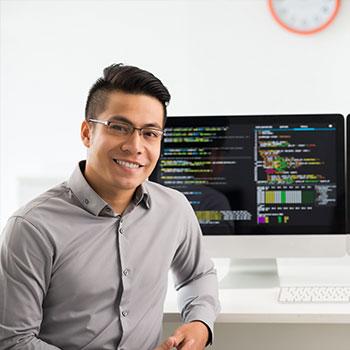 A man siting in front of a computer with code on it, smiling to the camera