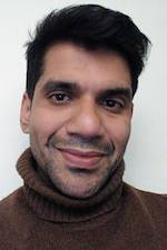 Omar Alam wearing a brown turtleneck sweater smiling at the camera