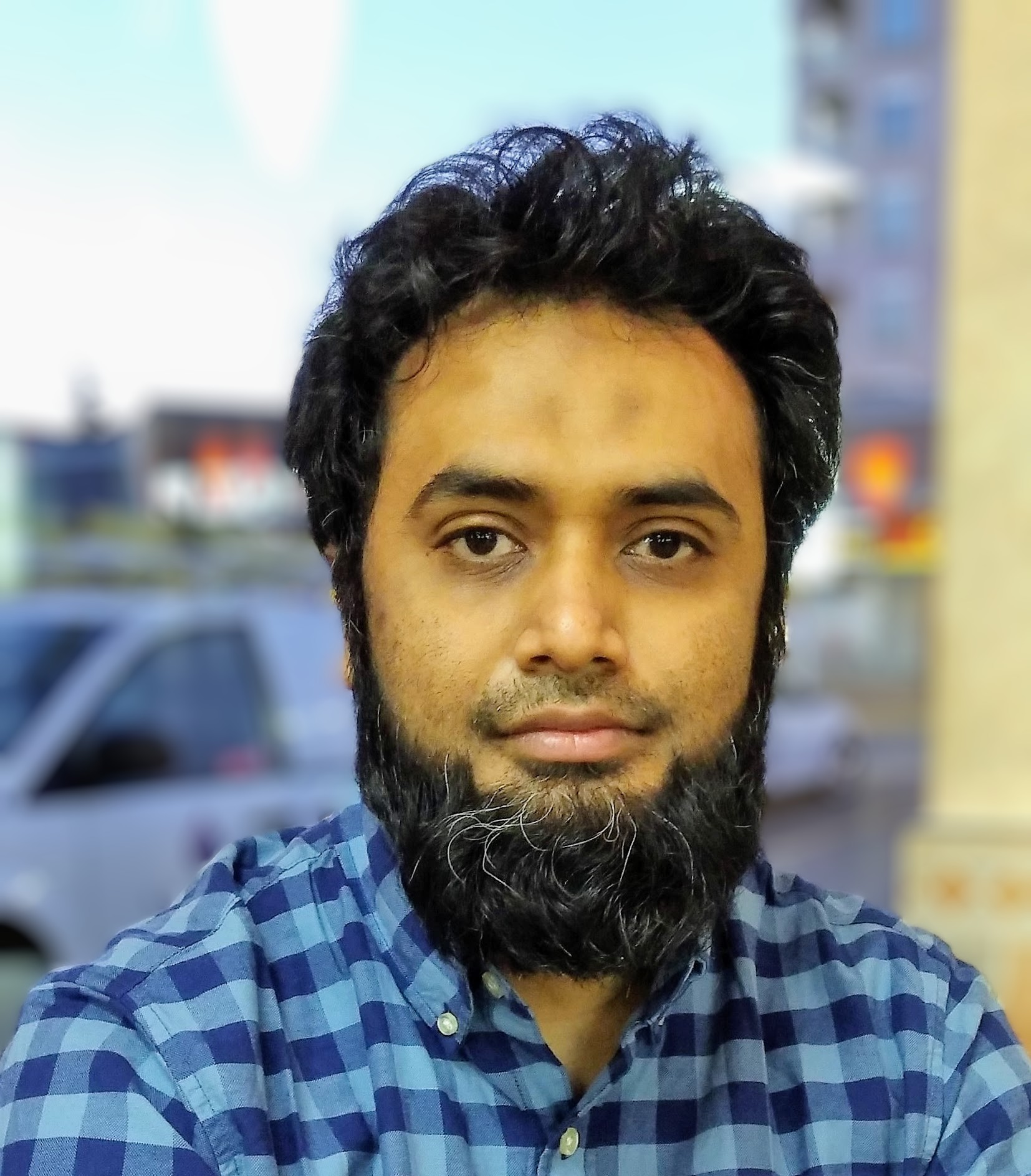 Quazi Rahman wearing a blue plaid button up shirt, looking at camera
