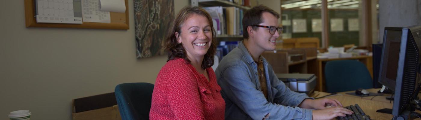 A professor working with a student on a computer and smiling