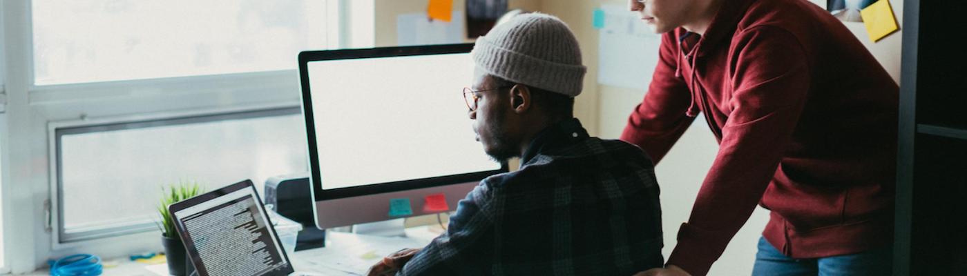 2 men working at a 2-screen computer together