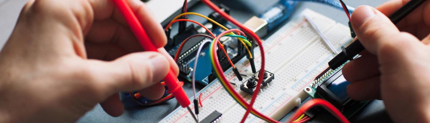 Someone's hands working on a circuit board with multiple red wires