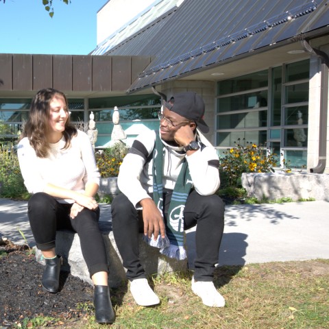 Two students sitting together outside of Otonabee College.