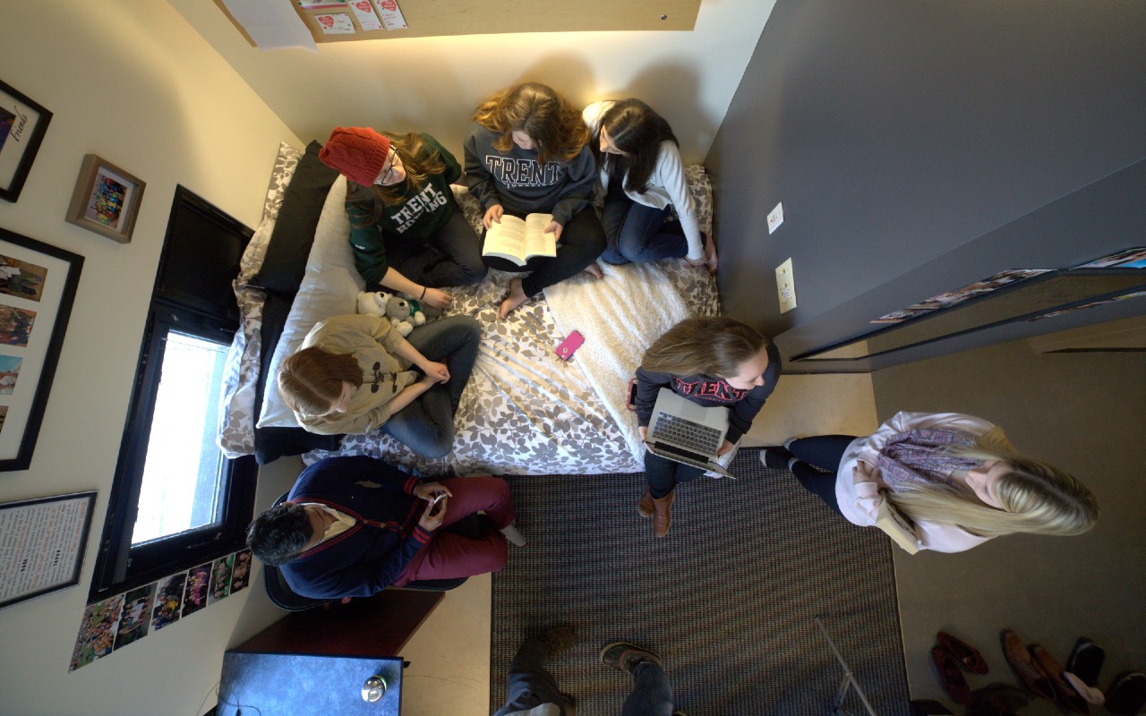 An overhead photo of a group of students sitting on a bed in a Gzowski College residence room.