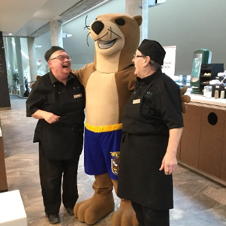 Two cafeteria employees posing for a picture with Otonabee's mascot Ottie the Otter.