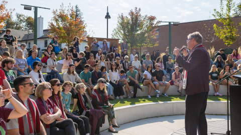Man on mic speaking to group in outside amphitheater