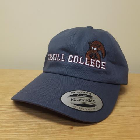 A navy blue baseball cap. The words "TRAILL COLLEGE" are written in white across the front of the cap and a brown squirrel is sitting above the lettering.