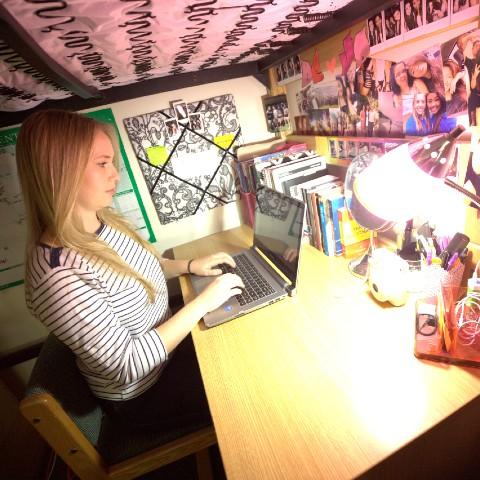 A Champlain College student typing on her computer in her residence room.