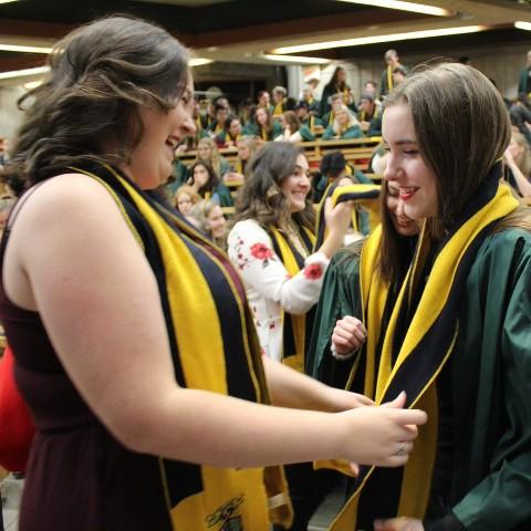 two people smile at each other at a scarfing ceremony where a fellow puts a scarf over a new student.