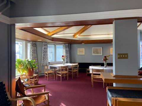 Traill College's Senior Common Room. The room is decorated in a 1960s style with large windows, exposed wood beams along the ceiling, and vintage wooden furniture.