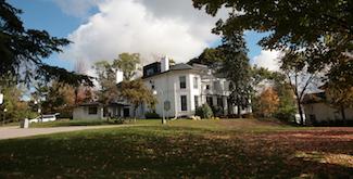 Scott House, a large white Victorian home surrounded by a green lawn and colourful autumn leaves.