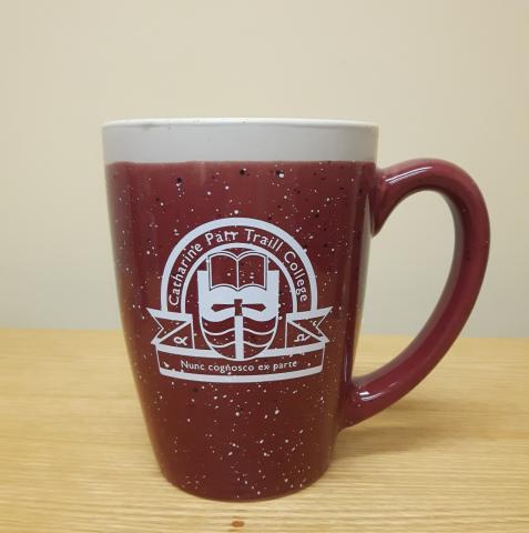 A maroon and off-white speckled ceramic mug with a white Traill College logo in the centre.