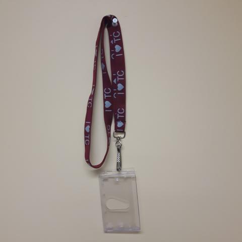 A maroon lanyard with "I HEART TC" printed along its length. There is a clear plastic card holder clipped to the end of the lanyard.