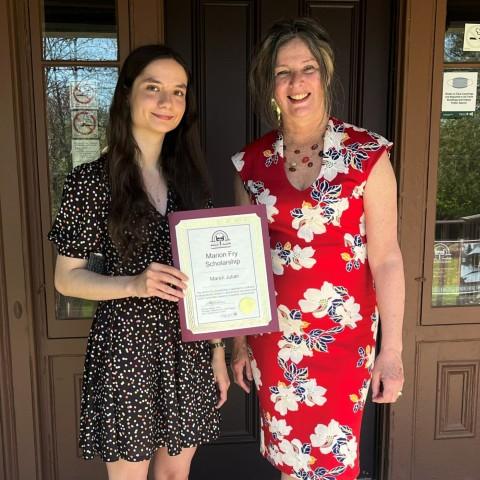 A Traill College student holding a Traill College award certificate and standing next to the Vice President of Colleges at Trent.