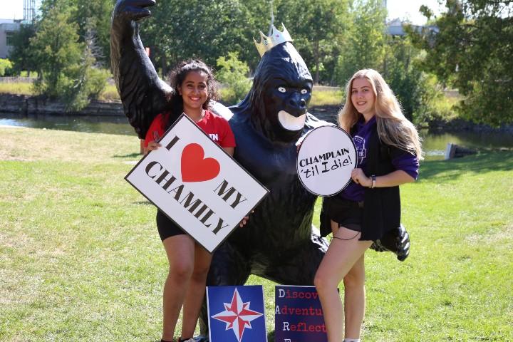 Two Champlain students posing and holding signs with PAX the Gorilla