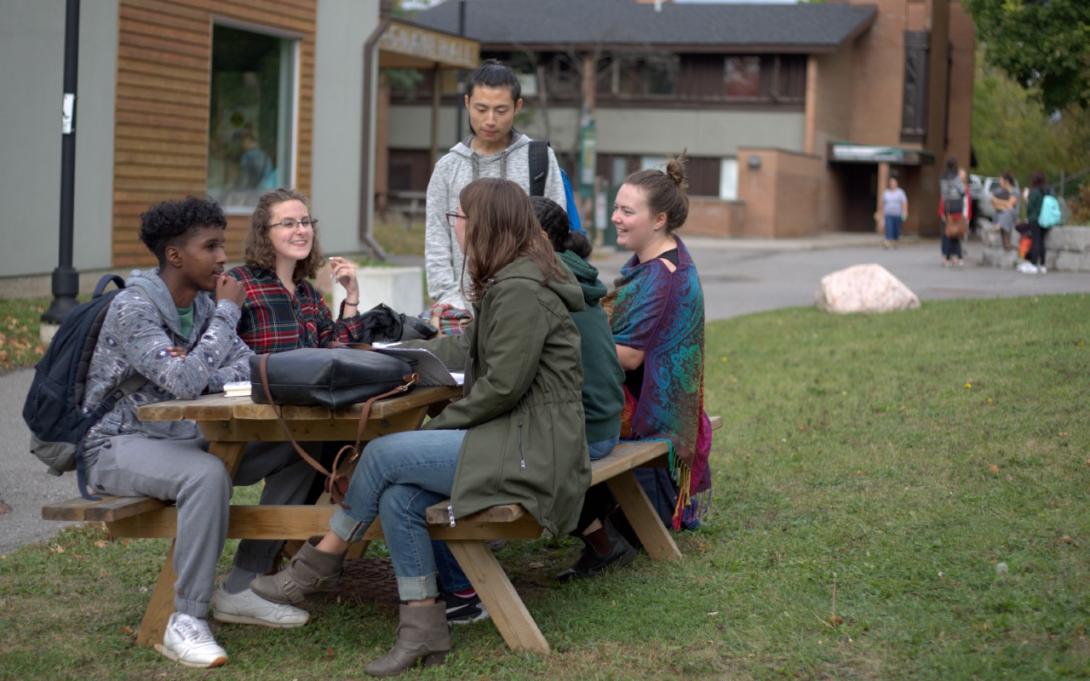 Six students sit around a picnic bench outside Bagnani Hall at Traill College.
