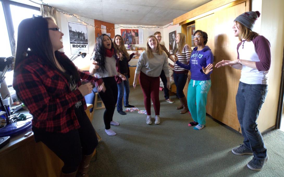 A group of students dancing together in a Lady Eaton residence room.