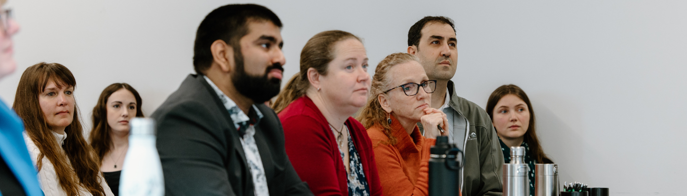 4 people sitting in a row listening to a presentation.