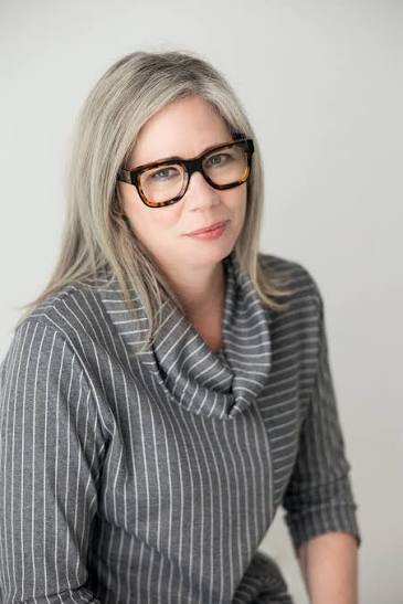 Female faculty Stephanie Rutherford looking at the camera. Silver hair, brown glasses, grey top