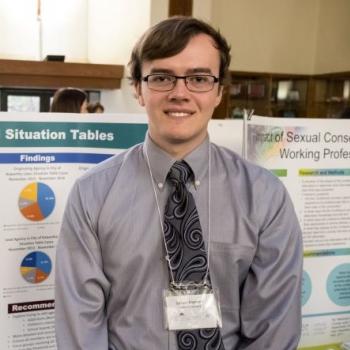 Student community-based researcher standing in front of his poster at the Celebration of Research.