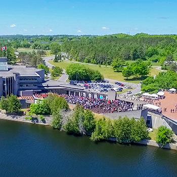 Aerial view of the Bata library and the Otonabee river during a convocation ceremony in the summer sun