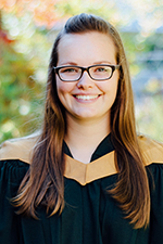 Eliza McColl smiling at the camera wearing a convocation gown with a gold hood