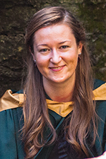 Kayla Goguen smiling at the camera wearing a convocation gown and gold hood