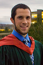 Peter Vice smiling at the camera wearing a convocation gown with copper hood, Bata Library in the background