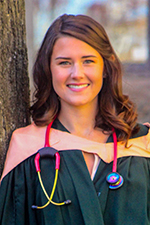 Kennedy Sage smiling at the camera, wearing a convocation gown with apricot coloured hood and a pink stethoscope 