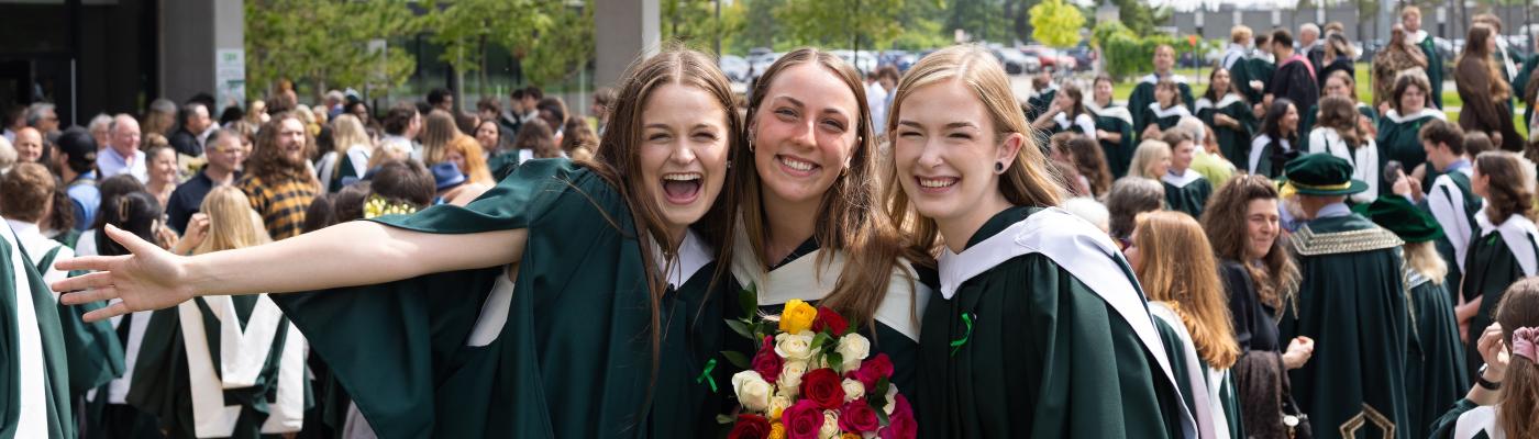 Three graduates standing outside smiling with their hands in the air