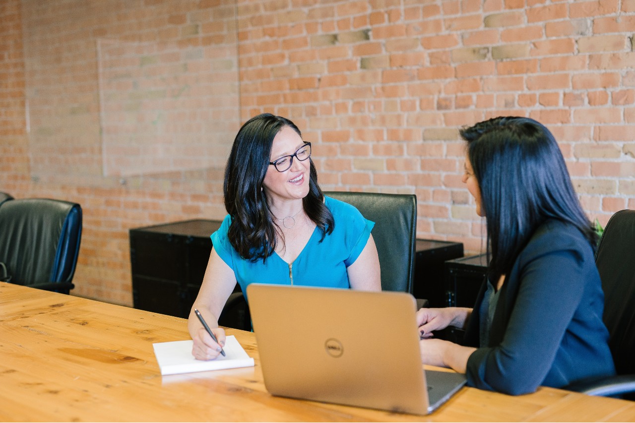 Woman in teal t-shirt sitting beside woman in suit jacket. Photo by Amy Hirschi on Unsplash