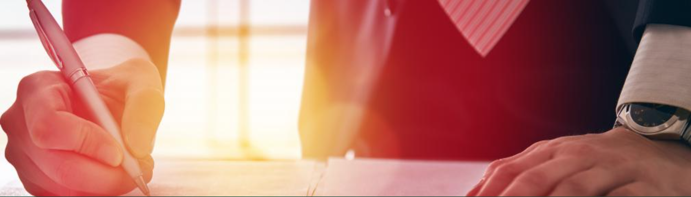 Man in a suit standing over desk writing on paper