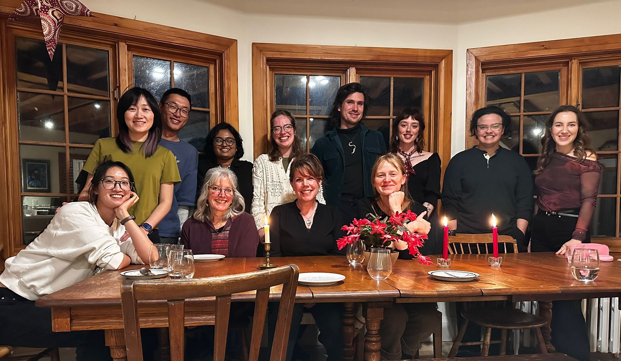 twelve students sitting and standing on one side of a table smiling at the camera