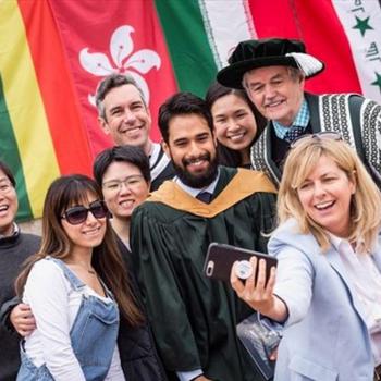 Group of staff and graduating students celebrating convocation day with flags in the background