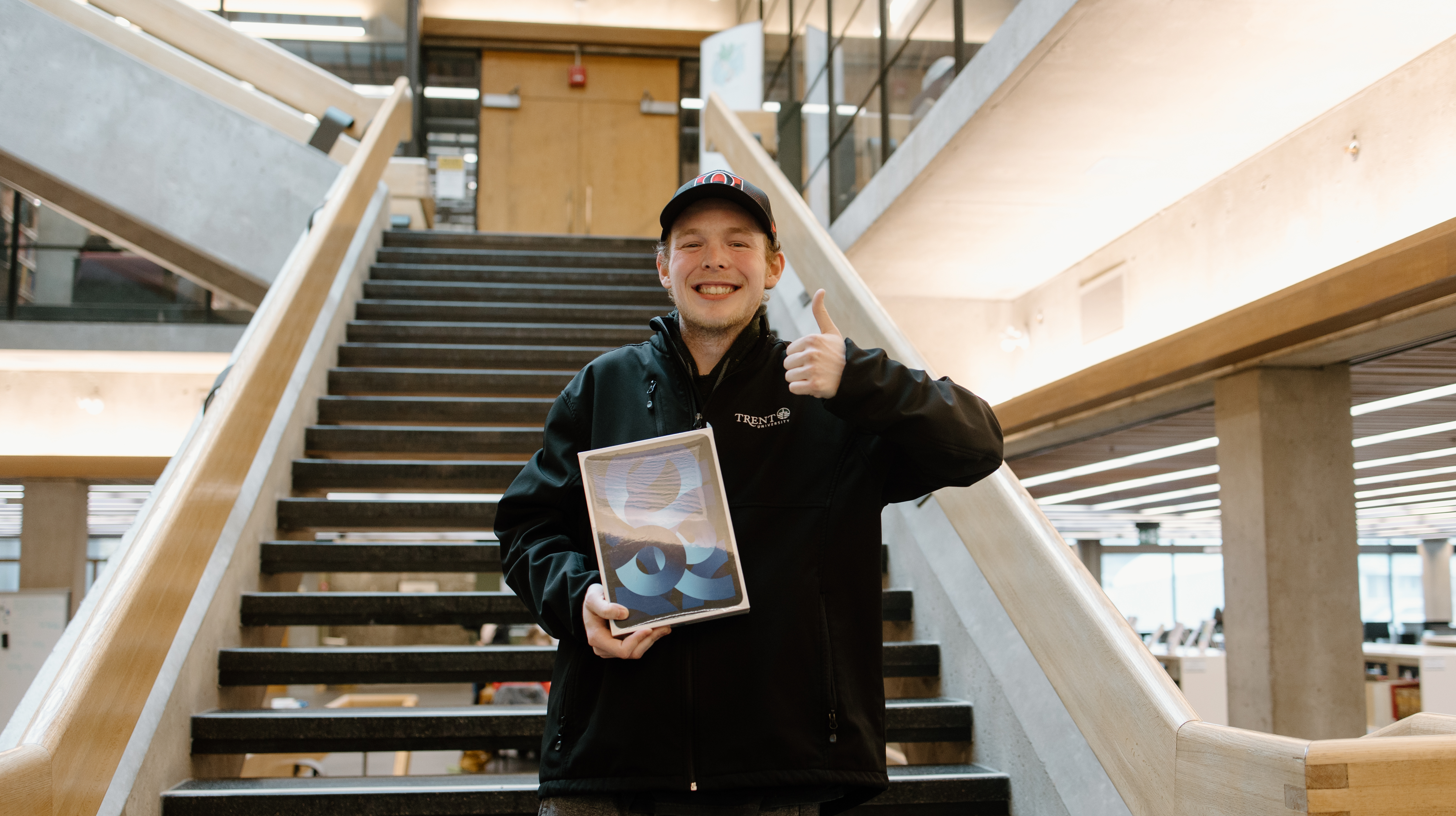 Smiling student holding an iPad and giving a thumbs up.
