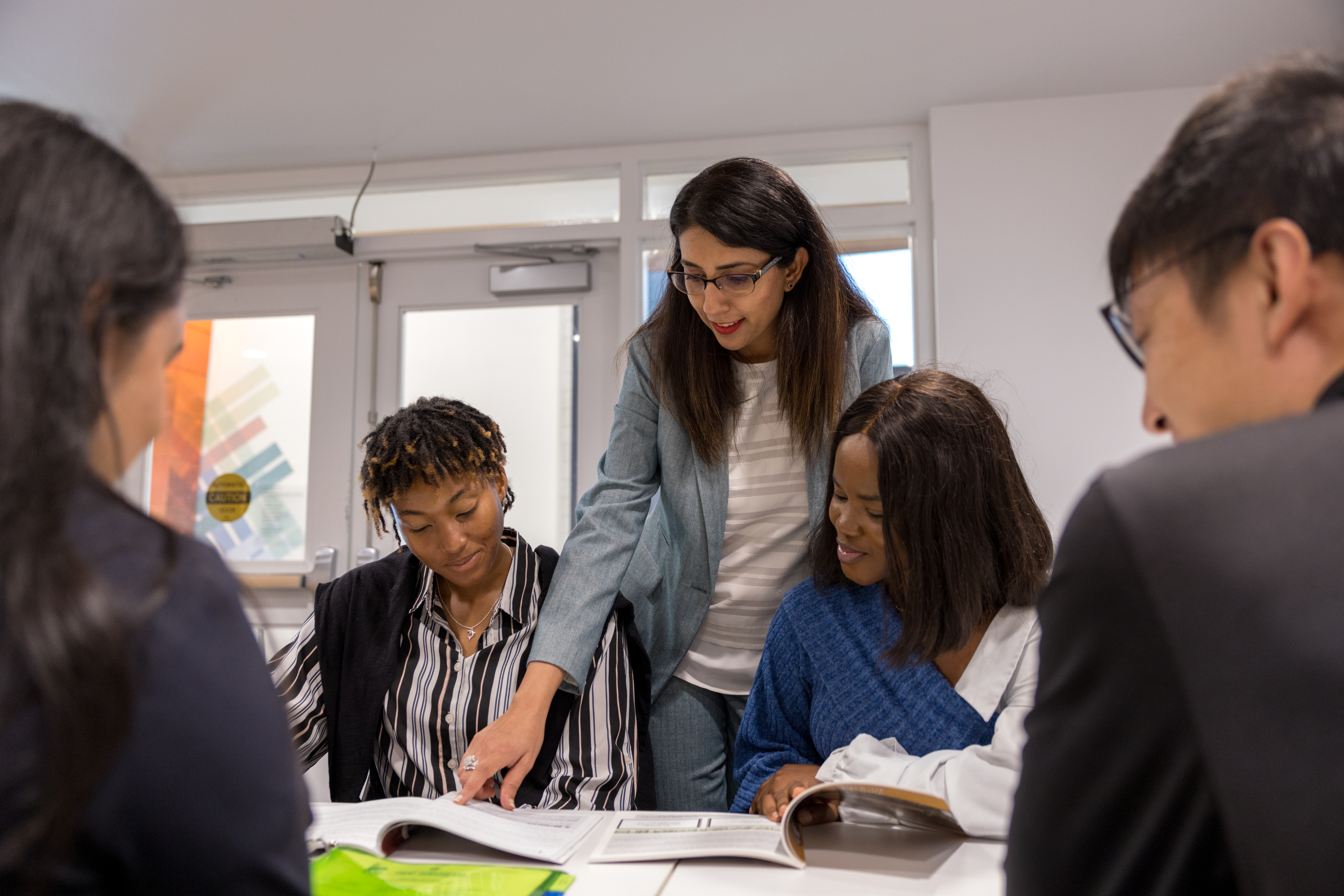 A professor is leaning over a group a student who is sitting, showing them something on a page in front of them.