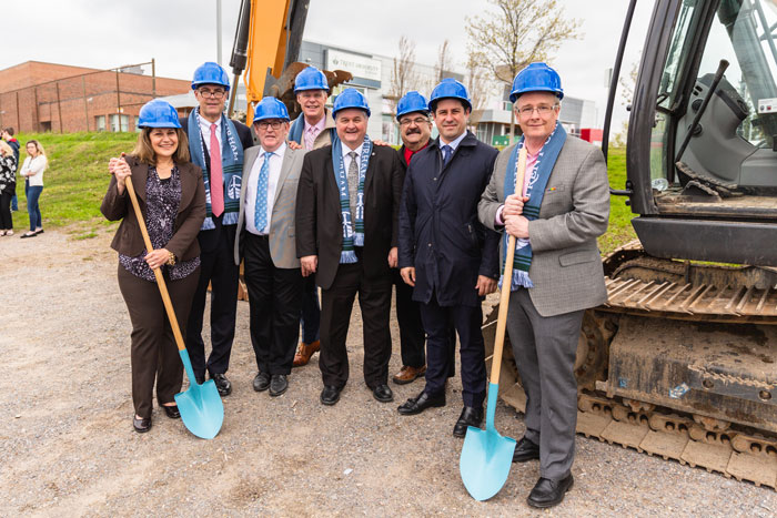 Dignitaries and VIP's hold shovels to the ground as they stand in front of a tractor at the site of the Trent University Durham GTA expansion. 