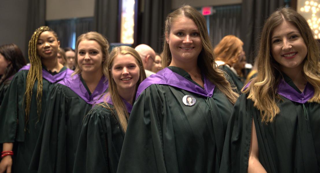 Group of students smile together in green graduation gowns
